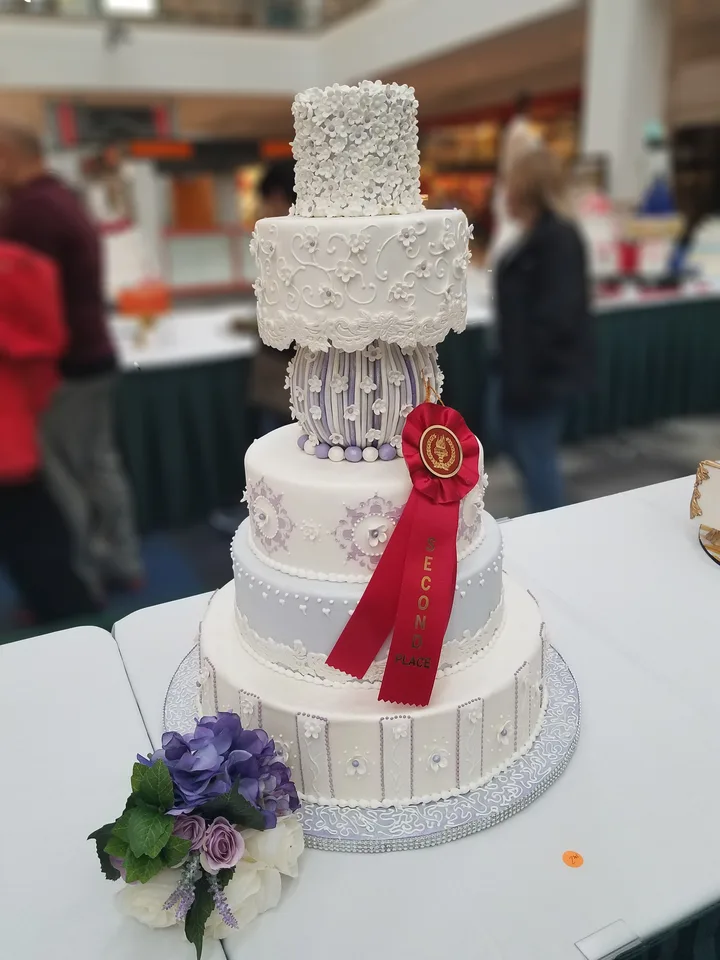 Tiered cake with a first-place ribbon, lace piping and purple flowers