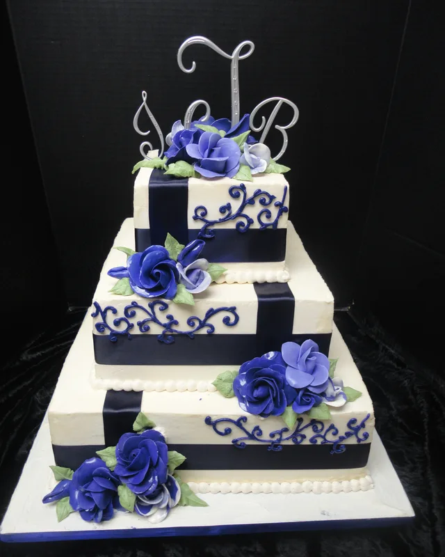 Square wedding cake with navy ribbon, blue sugar roses and a monogram topper