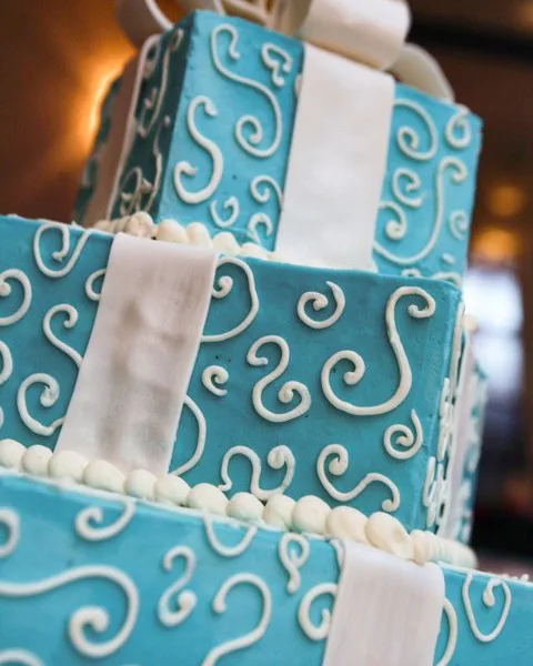 Close-up of a teal sculpted gift-box cake with white piped scrolls