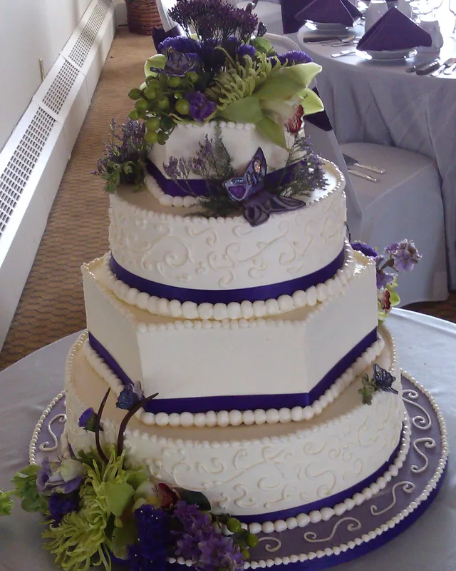 Hexagonal tiered cake with purple flowers and piped scrollwork