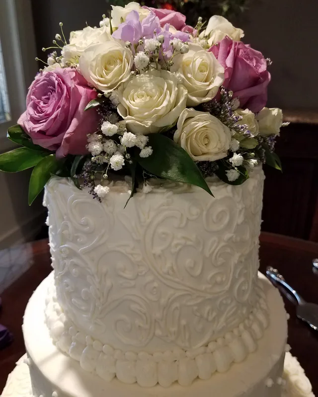 Tall white cake with piped scrollwork and a bouquet of roses