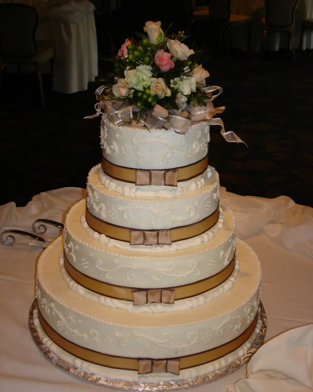 Round tiered cake with gold ribbon and a fresh flower topper